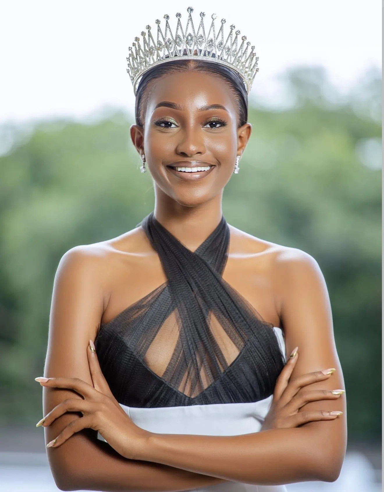 A crowned titleholder with her arms folded, outdoors
