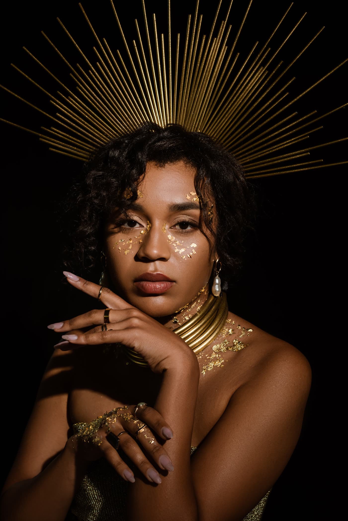 A woman in a golden headdress and gold leaf makeup