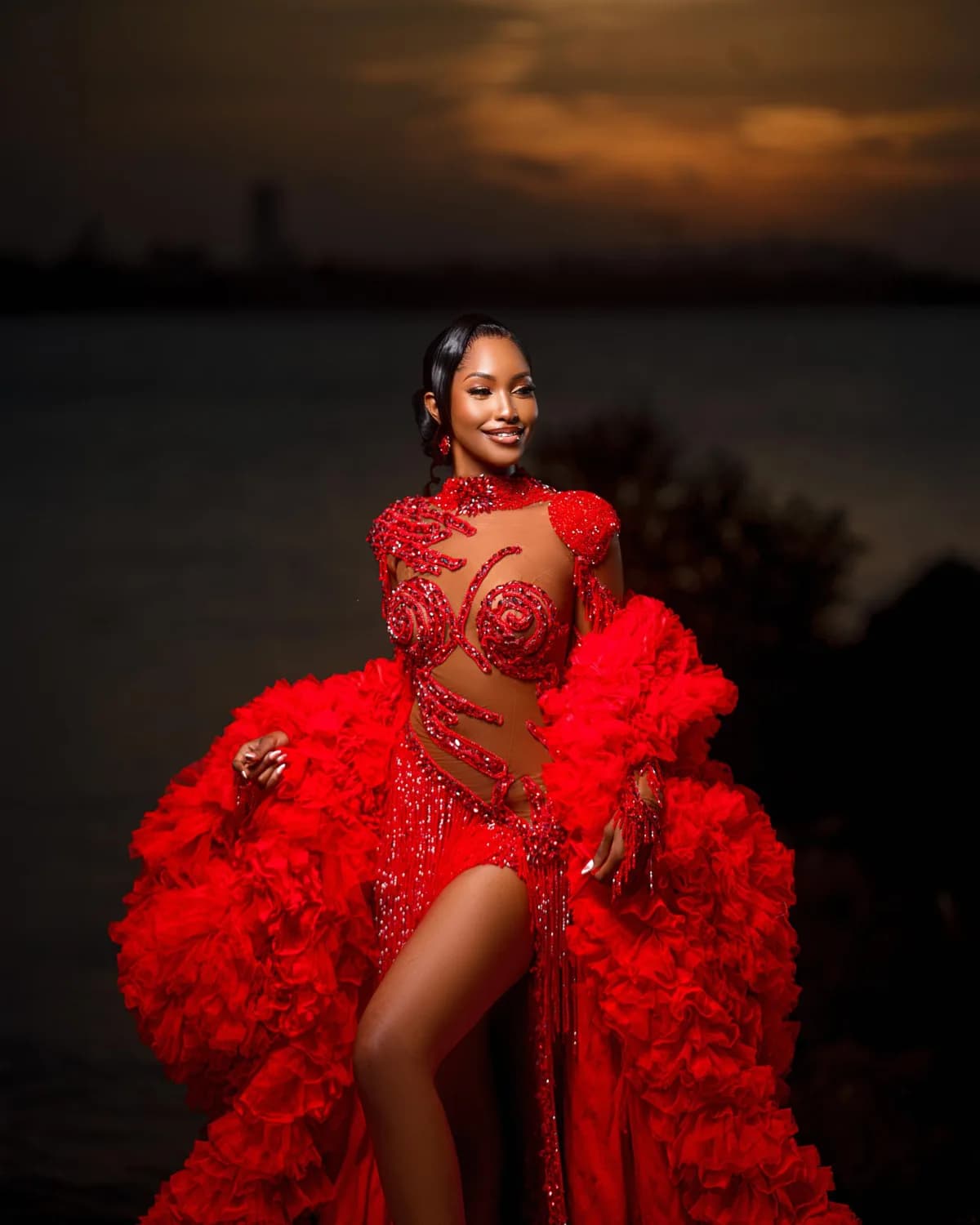 A woman in a red ruffled gown on the shore at sunset