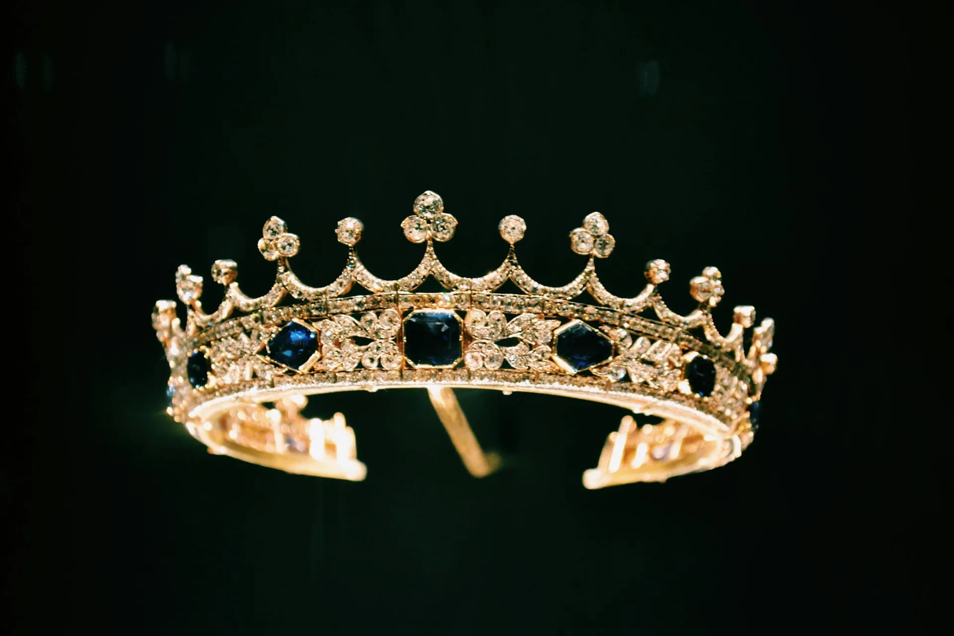 A jewelled gold crown set with sapphires, on a dark background