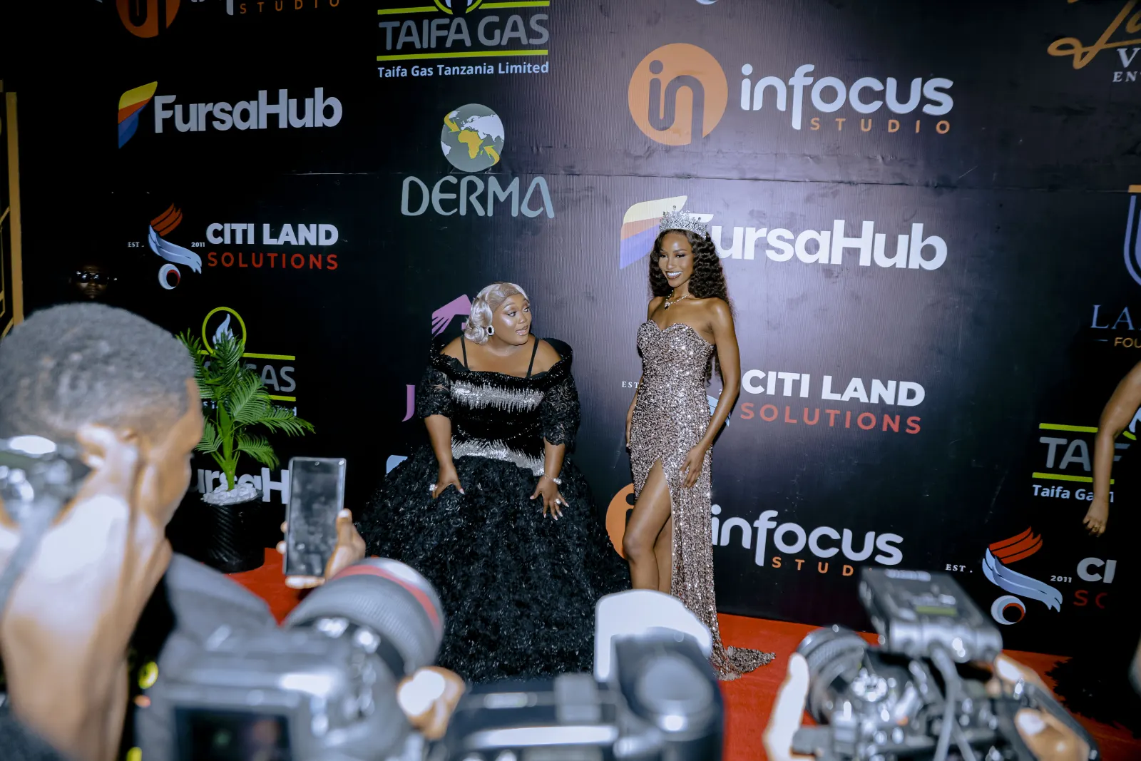 Two women in evening gowns on the carpet as photographers shoot