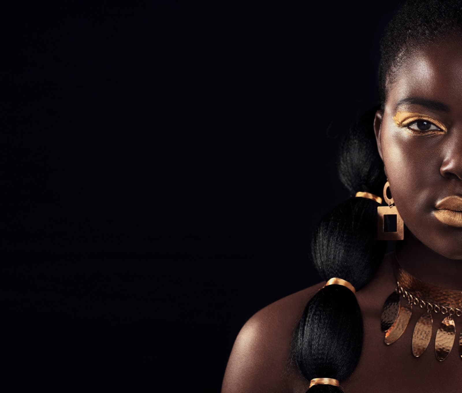 A young woman in gold jewellery against black
