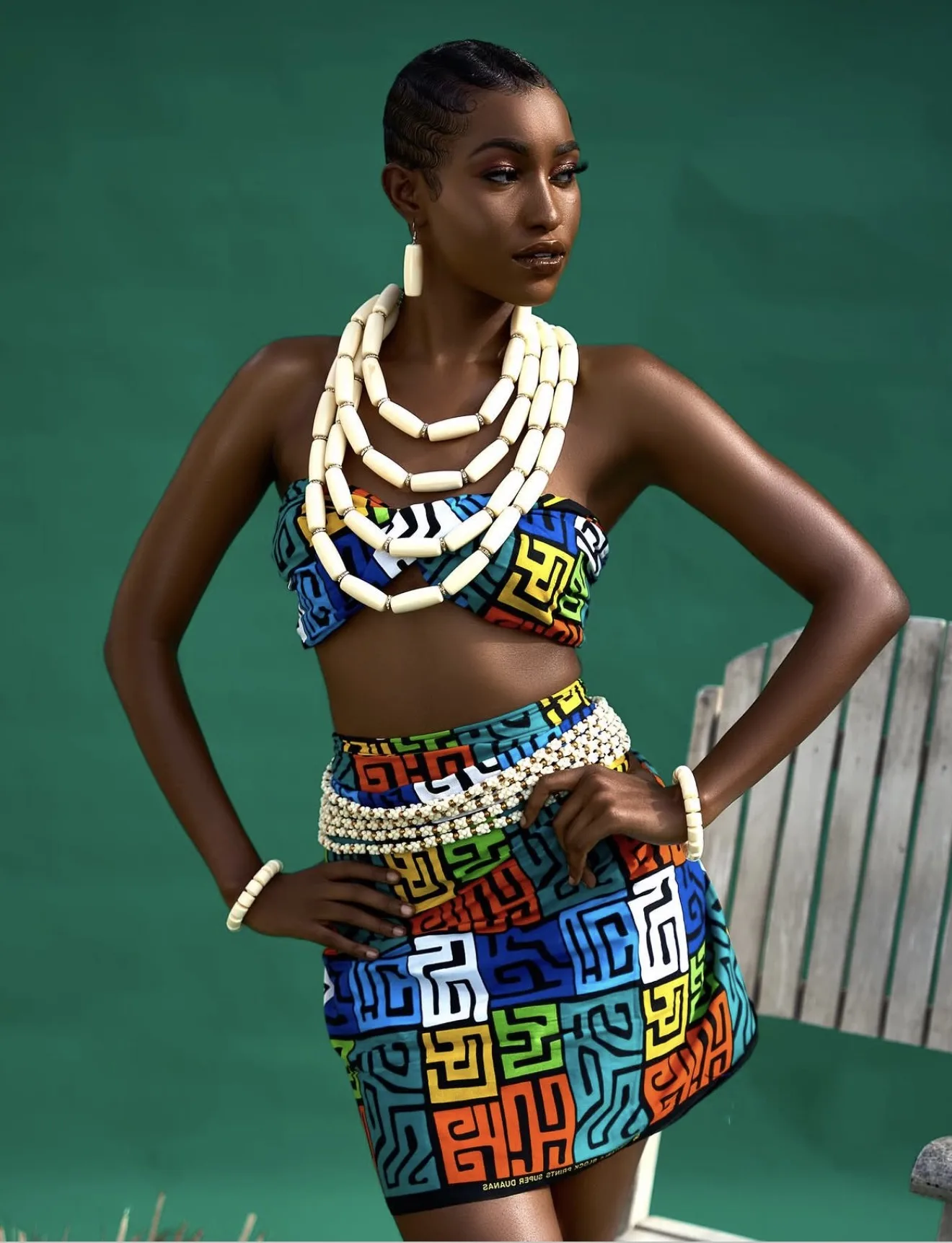 A woman in a kitenge print two-piece and layered bead necklaces